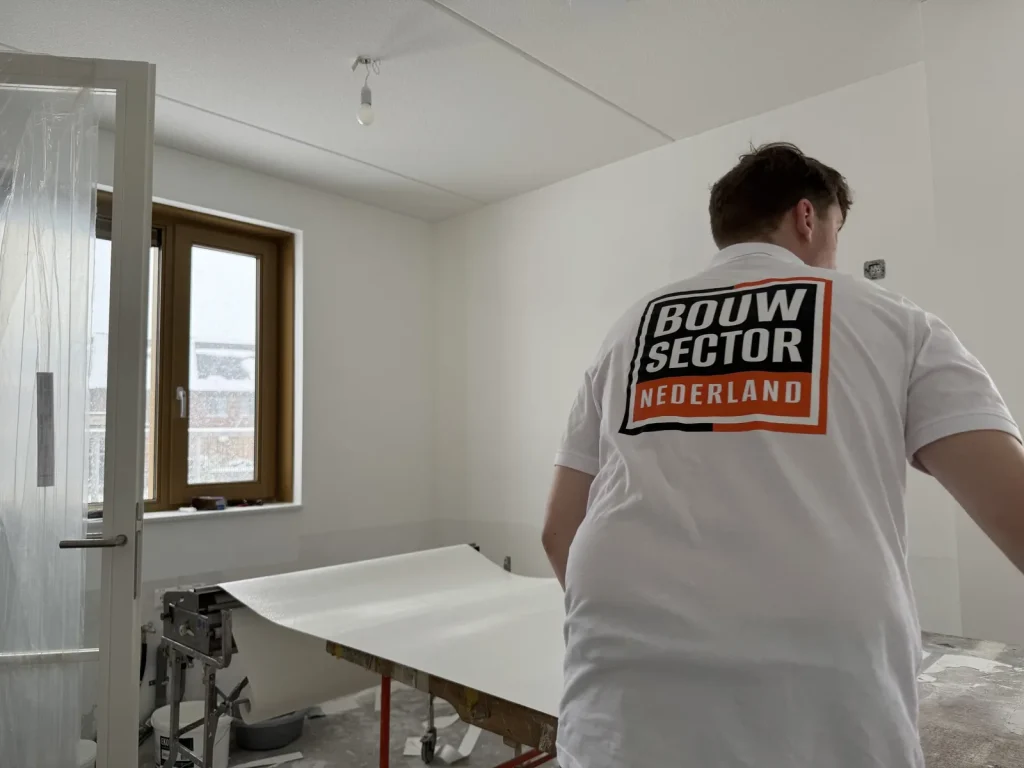 Behanger van Bouwsector Nederland rolt een baan renovlies uit op de plaktafel in een kale nieuwbouwkamer