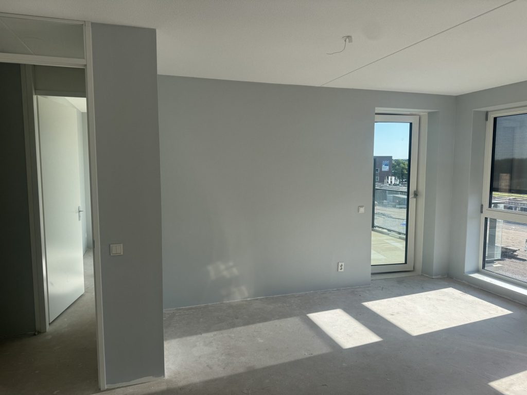 Appartement in aanbouw met lichtgrijs gesausde wanden en zon door de balkondeur