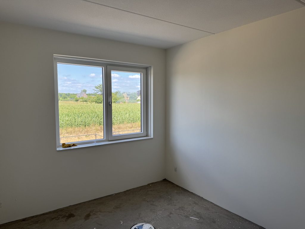 Kale slaapkamer met net afgewerkte witte wanden en een raam met uitzicht over het land