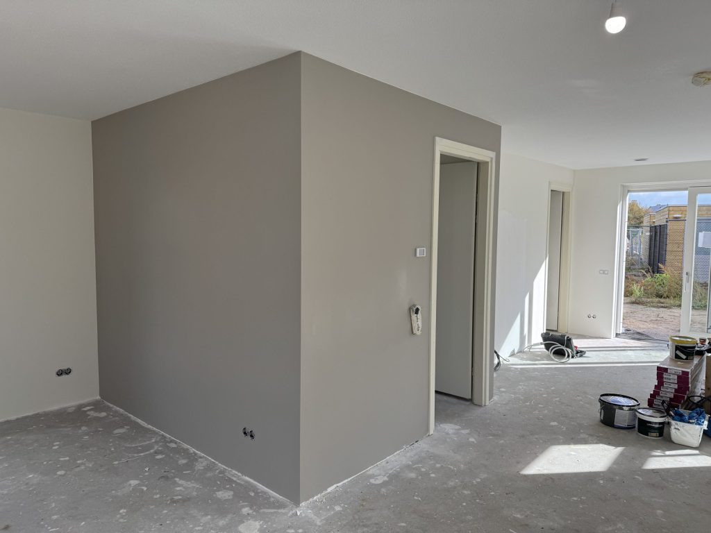 Strak afgewerkte grijze wanden rond een meterkast in een nieuwbouwwoning met kale betonvloer