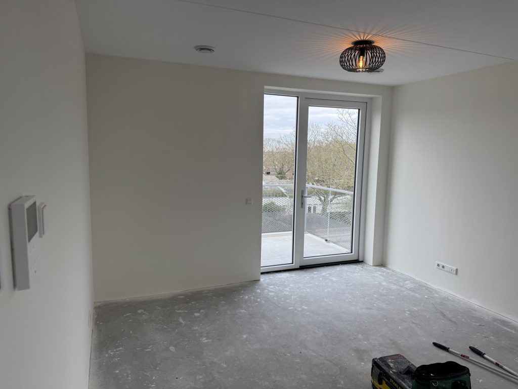 Lichte kamer in een nieuw appartement met glazen balkondeur en strak afgewerkte witte wanden