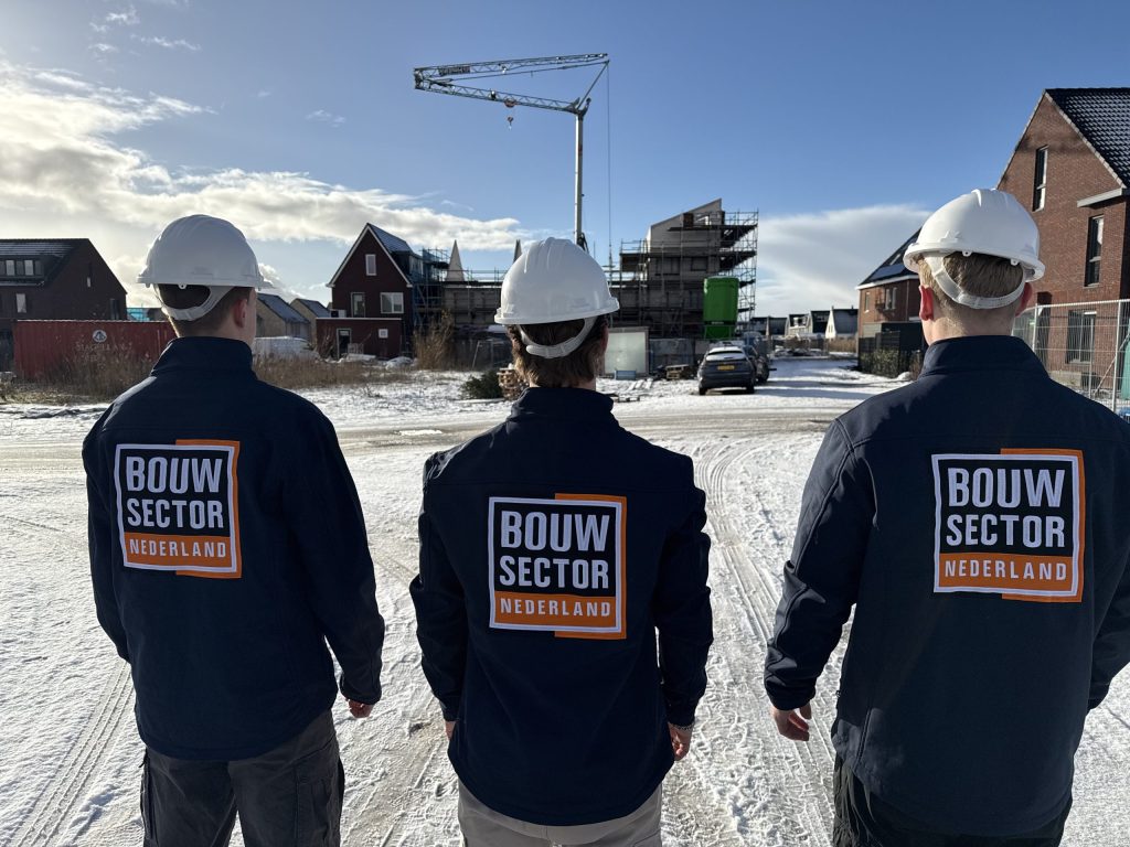 Drie collega's van Bouwsector Nederland met bouwhelm in een besneeuwde straat met nieuwe woningen